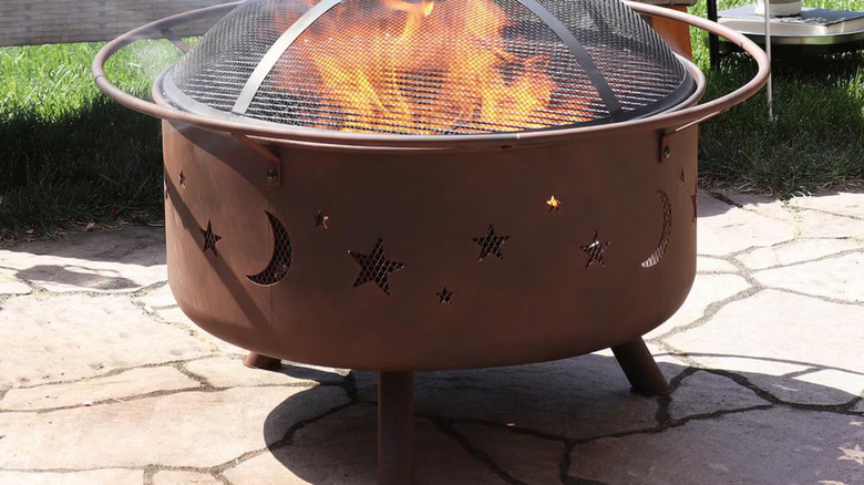 Bowl-style fire pit has spark-screen cover and feet to keep it out of direct contact with the ground.