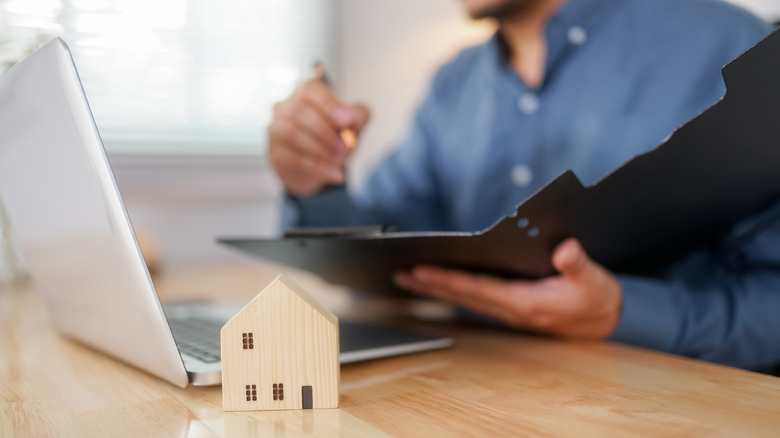 A person at a laptop with small wooden house in foreground