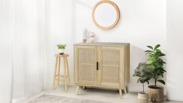 The Aldi accent cabinet in a room with a round mirror on the wall, a tall wooden stool, and a range of plants