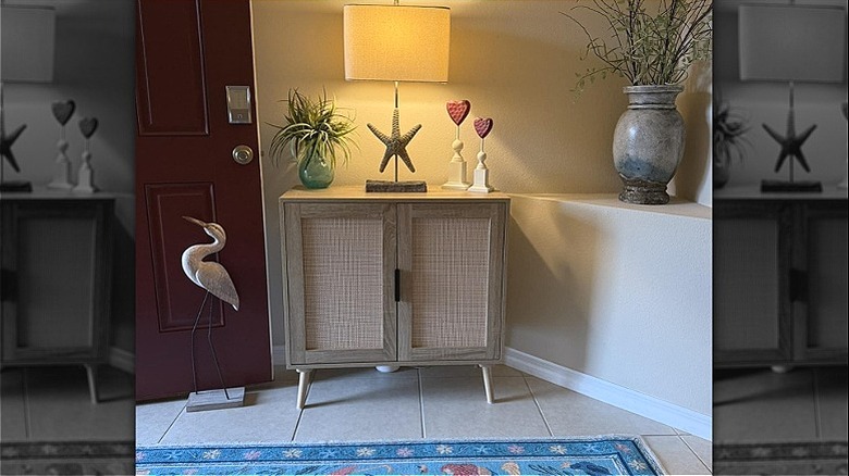 The Sohl Accent Cabinet from Aldi in a corner of a room with a lamp, a plant, and some decorative items on top