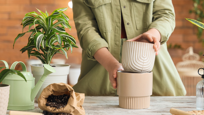 A woman in a light green jacket removing one plant pot from another