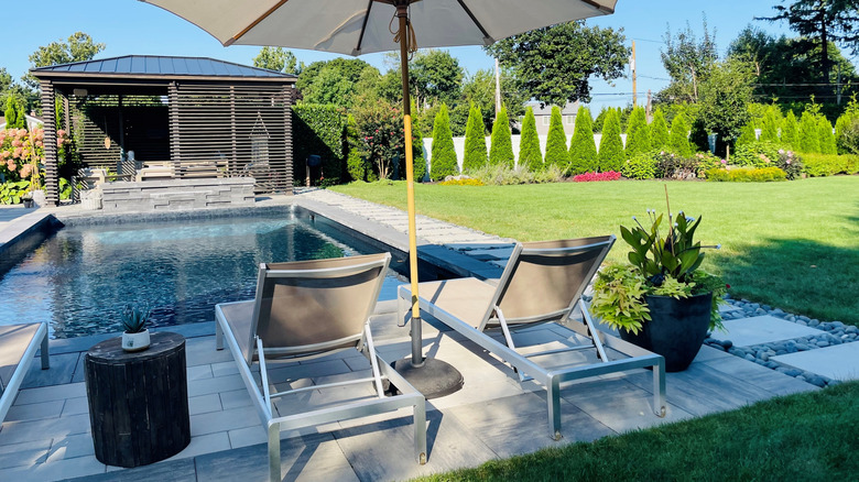 A beautifully landscaped backyard features a pool, pool house, lounge chairs, and umbrella.