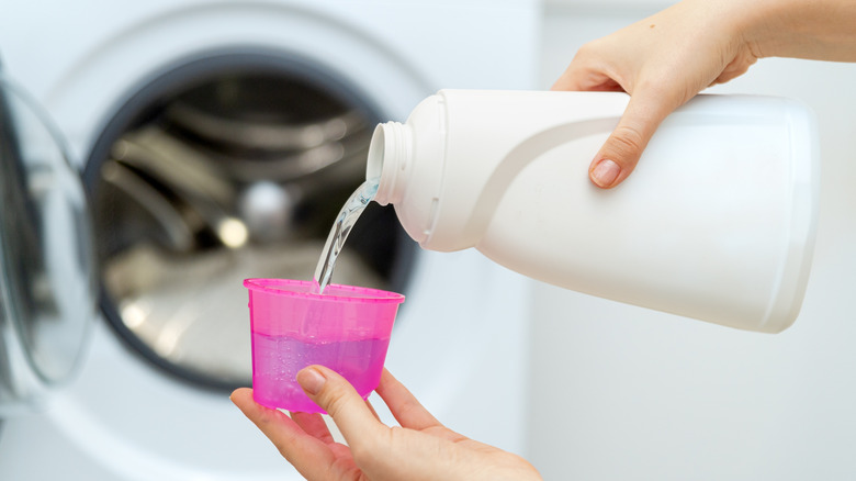 Close up of hand pouring liquid detergent in a cap, dryer in the background