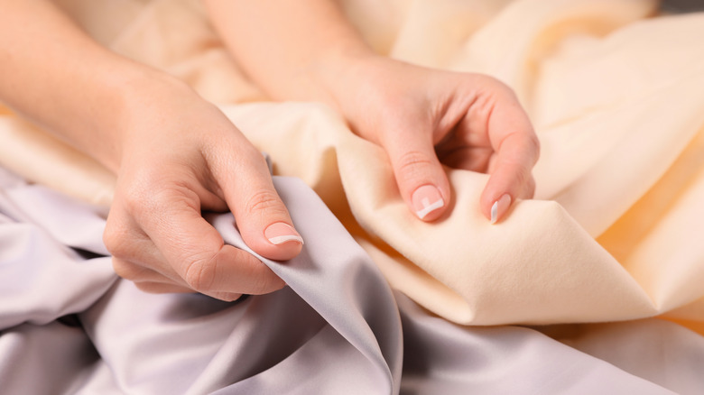 A person compares two bedsheet fabrics in different colors