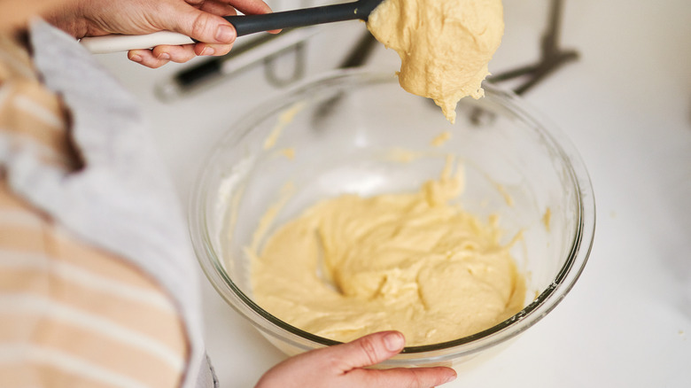 A person mixes ingredients in a clear glass mixing bowl
