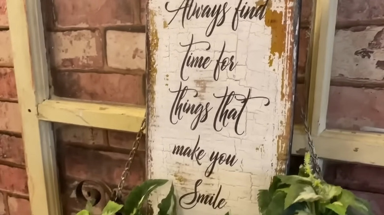 Decorative wood sign with a distressed, crackled finish propped near some plants