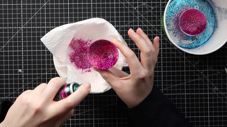 Woman holds a can of hair spray over a bowl of glittery Christmas ornaments