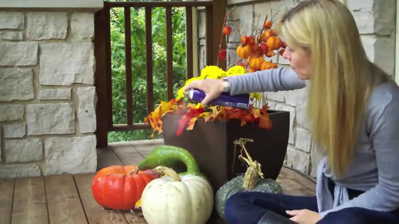 Woman in light blue shirt and dark blue jeans sprays decorative pumpkins and gourds with hairspray