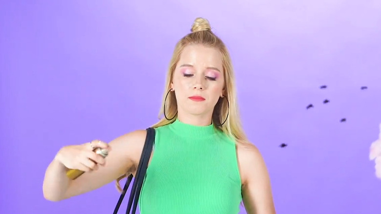 Blonde woman in green ribbed tank spraying hairspray around flies