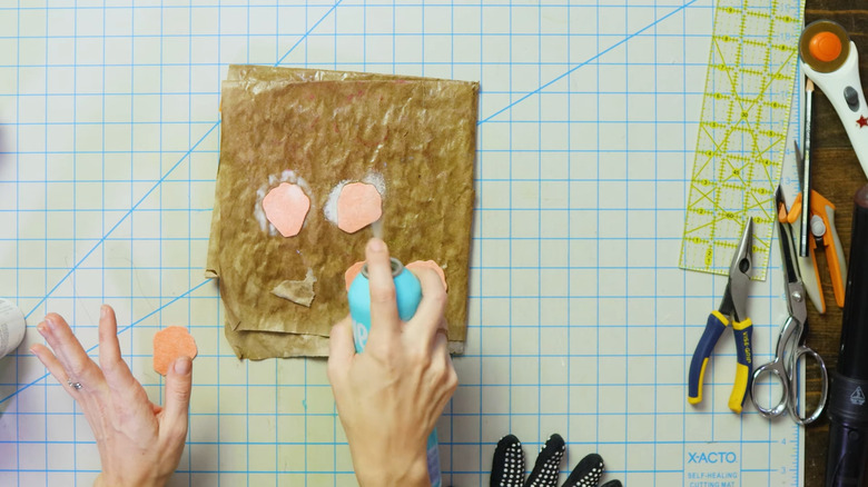 Woman sprays pieces of pink felt with hair spray on a crafting mat