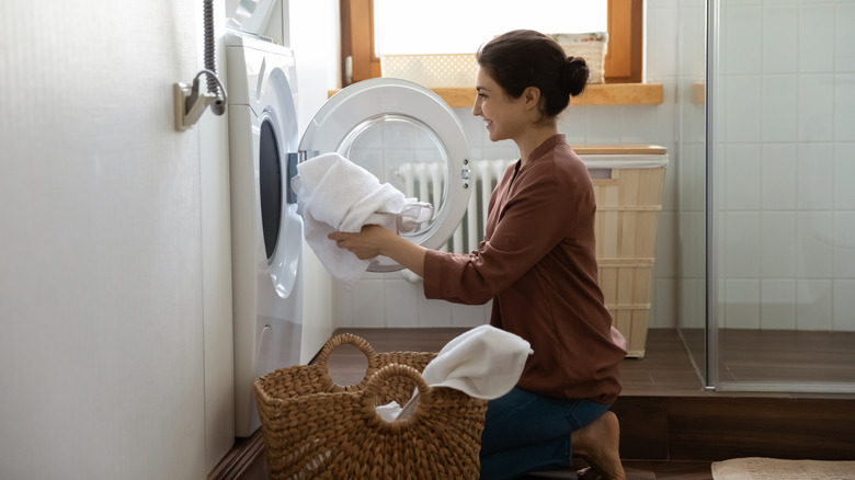 Woman putting in white towels in washing machine