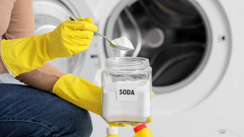 Gloved hands holding baking soda in a spoon near a washing machine