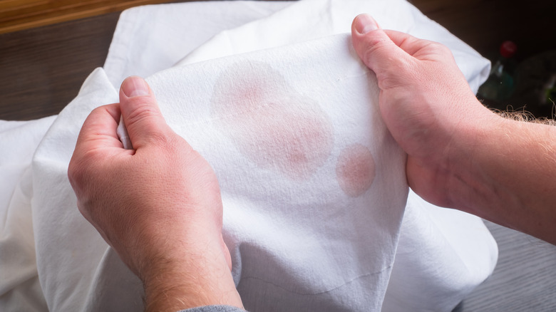 Man holding a white article with red wine stains