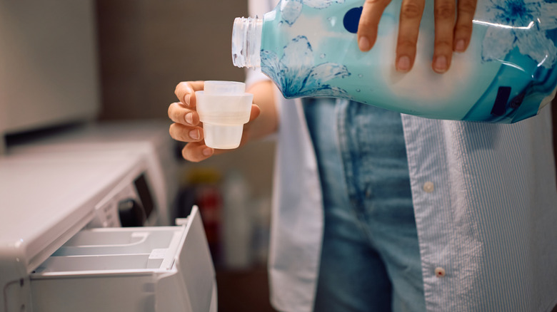 Woman adding fabric softener in washing machine compartment