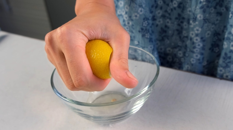 Hand squeezing a lemon in a glass bowl