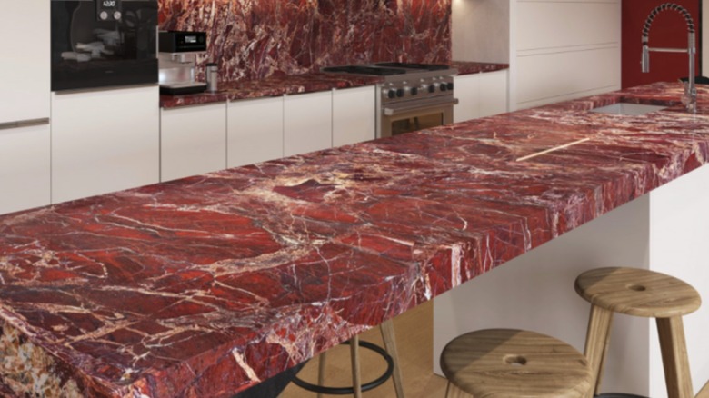 A kitchen with red marble island, countertops and backsplash and white cabinets