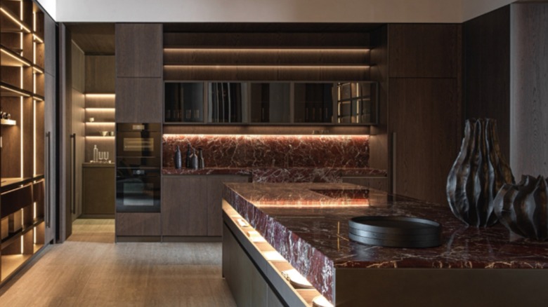 A modern kitchen with dark red marble countertops, dark wood cabinets, and mood lighting throughout