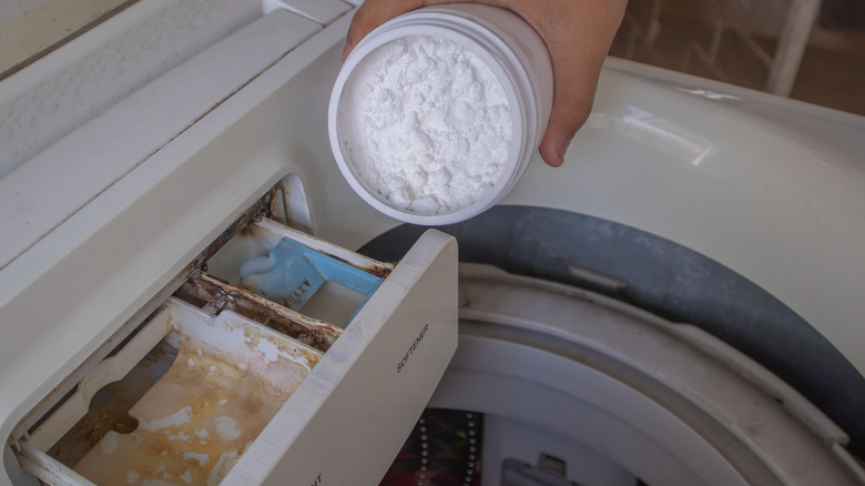 A person is shaking baking soda into the detergent and softener trays of a washing machine