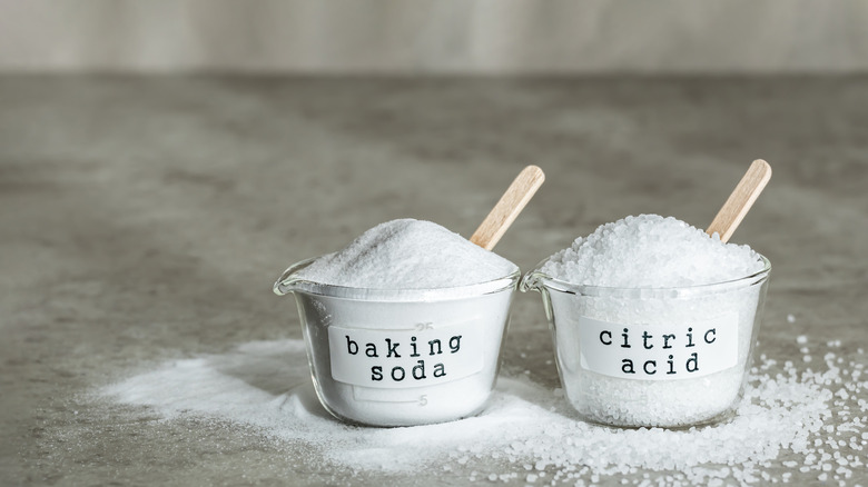 Cups of baking soda and citric acid sit side by side, each with a wooden scoop