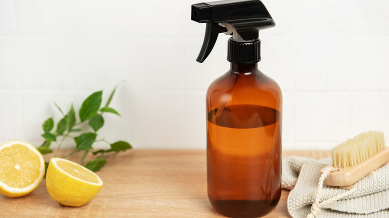 Cut lemons and a spray bottle with juice are shown with a brush and rag
