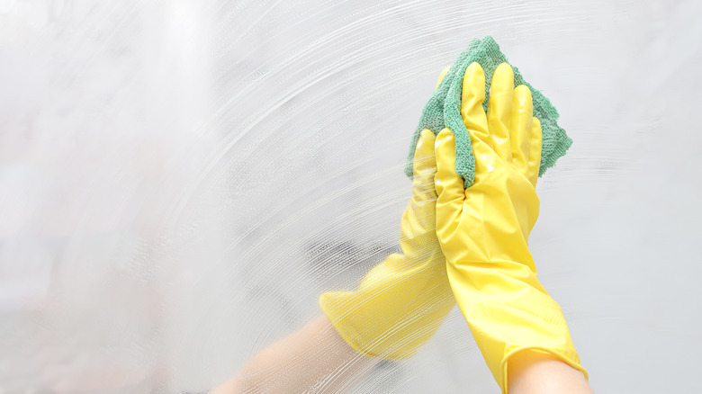 person cleaning mirrors with rag while wearing gloves