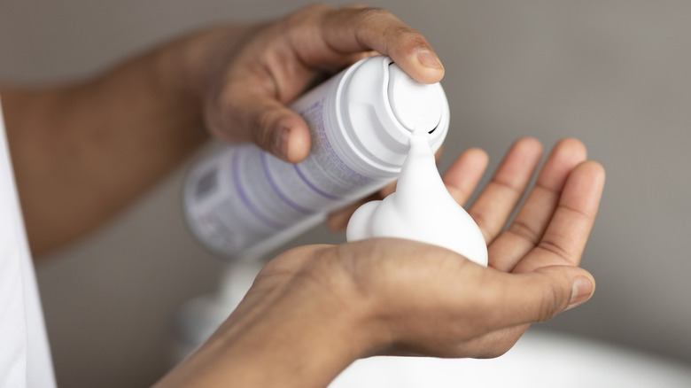 A hand spraying shaving cream into the palm of the opposite hand.