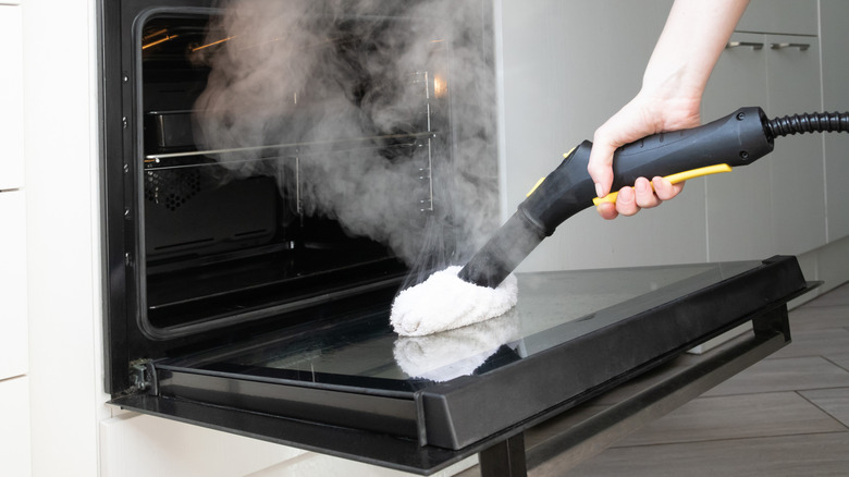A person using a steamer to clean the inside of their oven.