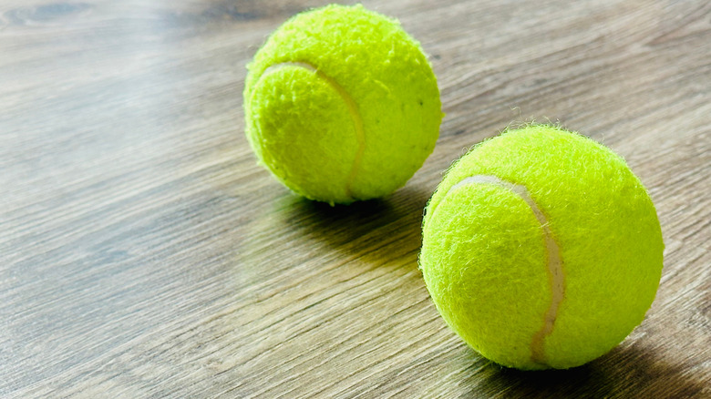 Two tennis balls sitting on the floor.