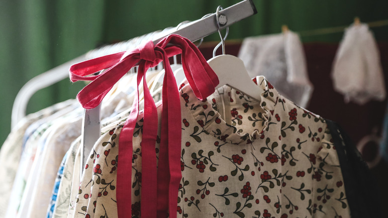 A red ribbon tied in a bow on a rack full of clothes hung on coat hangers.