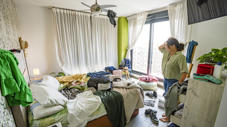 Upset woman head in hands contempling her messy bedroom