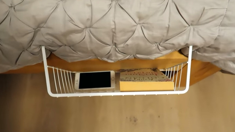 Book and iPhone resting in a under-shelf storage basket hung vertically on a bed frame