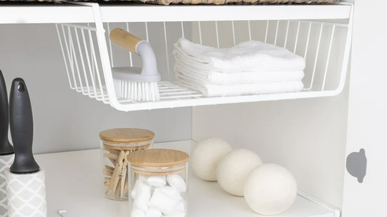 Rags and a brush in an under-shelf basket in a laundry room