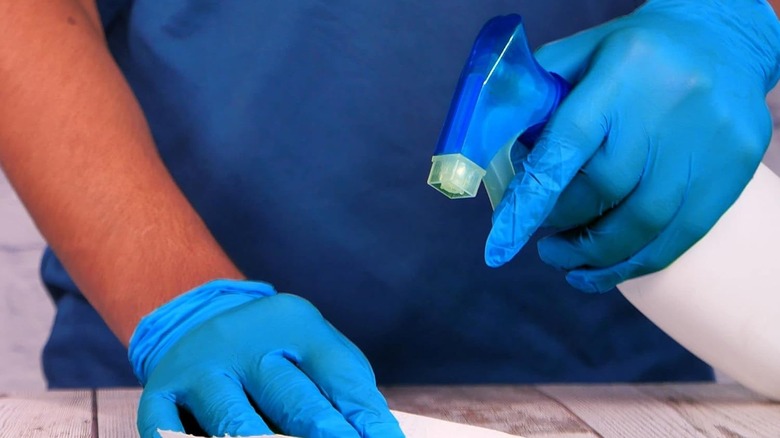 man with blue nitrile gloves cleaning wood table
