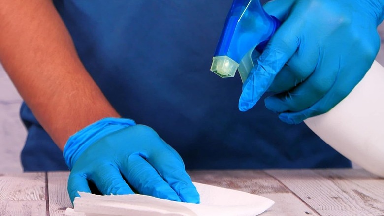 man with blue nitrile gloves cleaning wood table