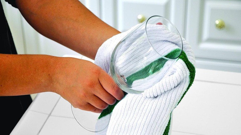 Person cleaning wine glass with microfiber white and green bar towel