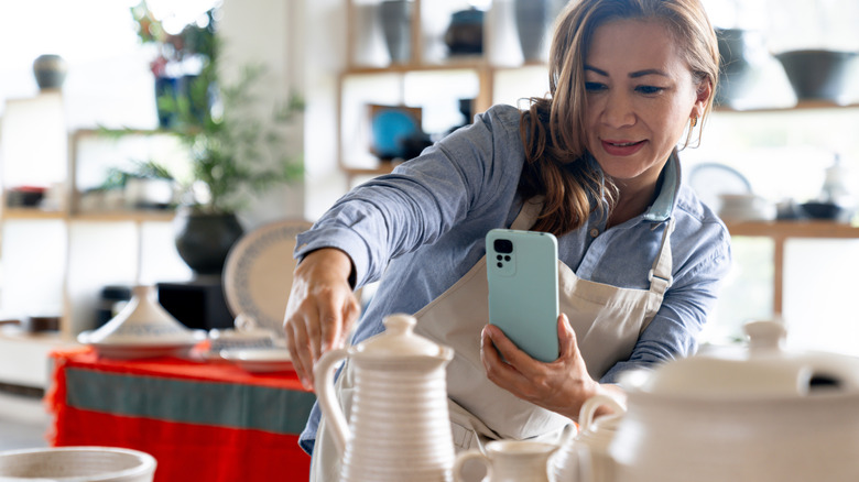 Woman using her phone to take a picture of pottery.