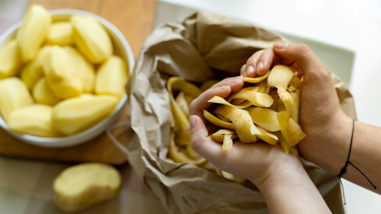 Hands holding potato peels over peeled potatoes