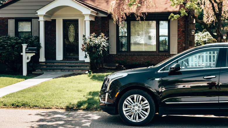 A black car parked in front of a brick home