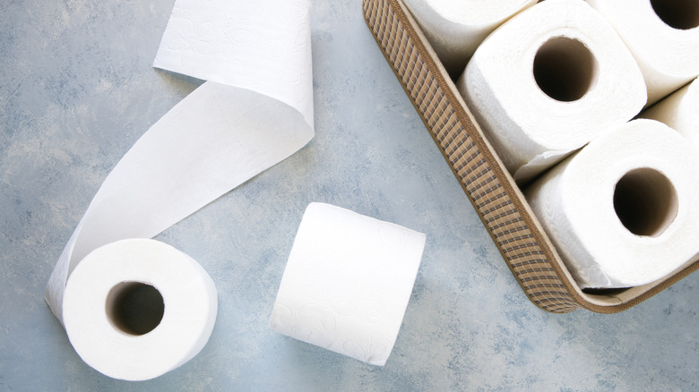 Basket of toilet paper with a couple rolls out on the counter.