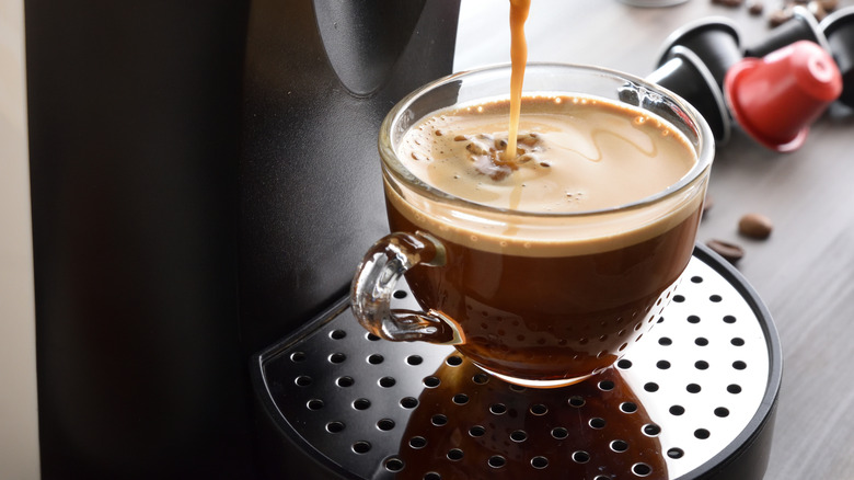 A coffee machine pouring coffee into a glass come with k-cups in the background