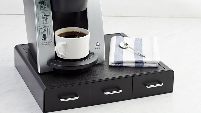 The Amazon Basics K-Cup Compatible Coffee Pod Storage Drawer with a coffee machine and a napkin and spoon on top