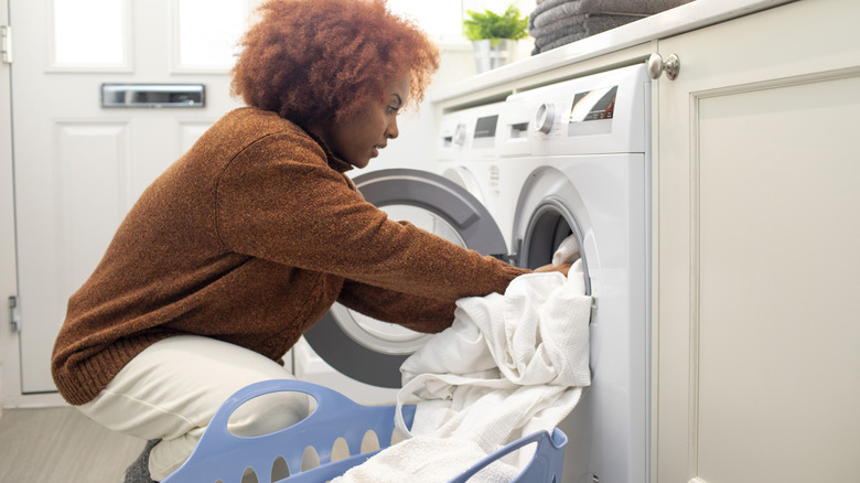 person doing their laundry, putting blankets in a washing machine