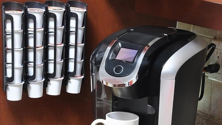 The Storagenie K Cup Holder hanging on a wall next to a Keurig coffee machine