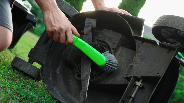 Person using a brush to clean the underside of a lawn mower