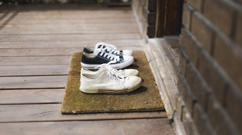 Sneakers sitting on a door mat on the front porch