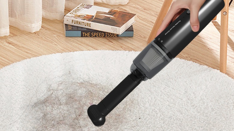 Hand holding a black cordless vacuum over a white rug