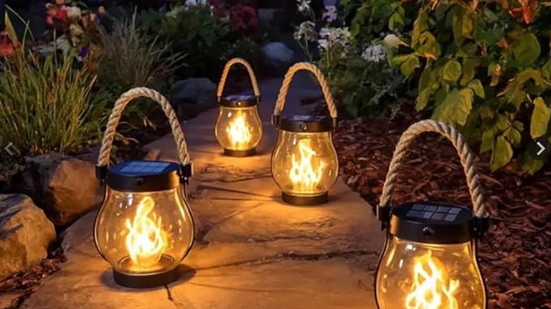 Four lit solar lanterns lighting up a dark walkway in garden