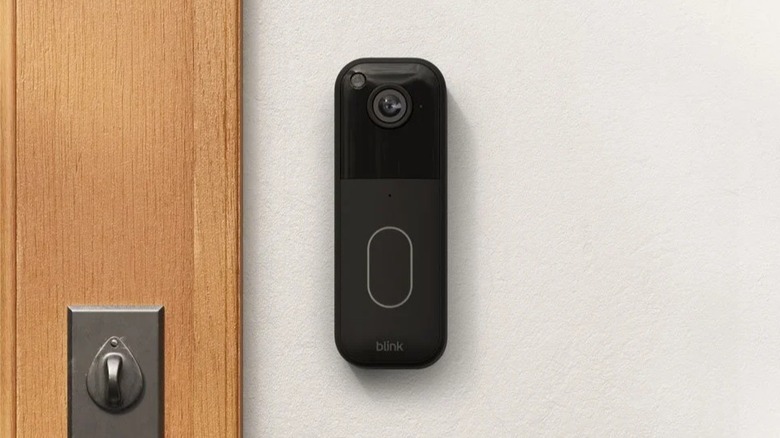 Black Blink video doorbell installed near a door on a white wall