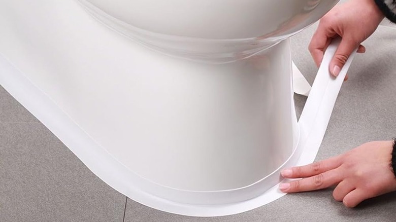 Person applying thick white caulk tape around toilet