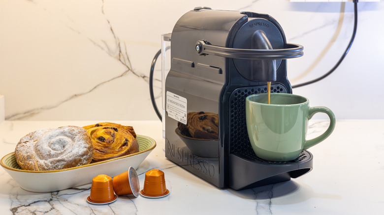 A coffee machine with a mug and some coffee pods on the counter
